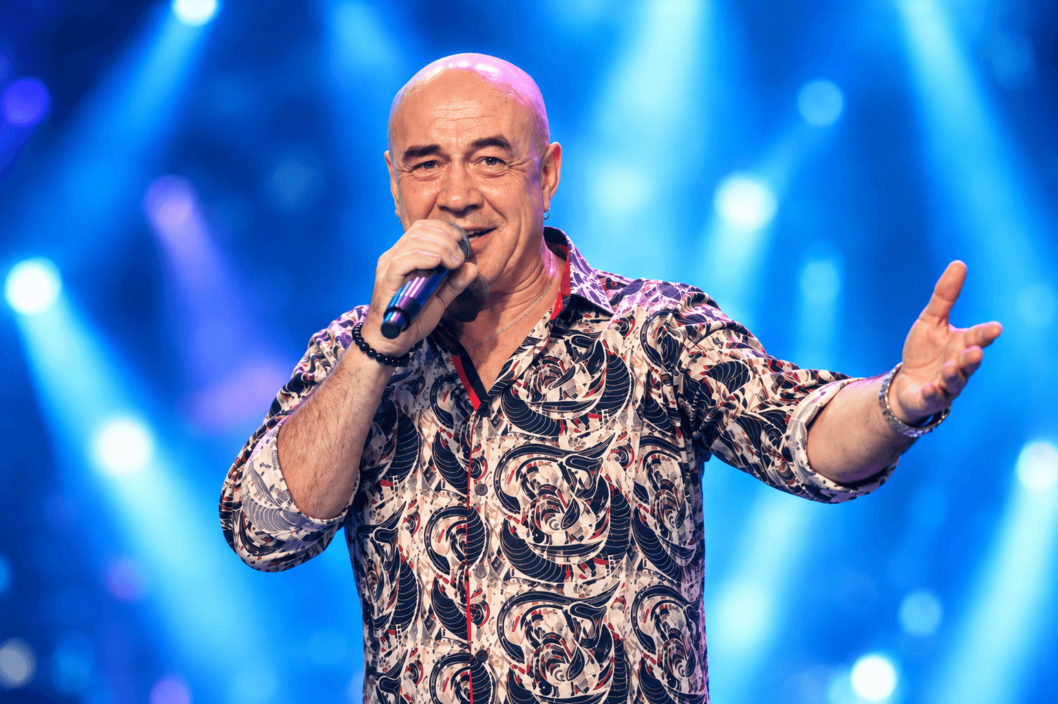 Oleg Sweet singing on a concert stage with two backing dancers in pearl dresses